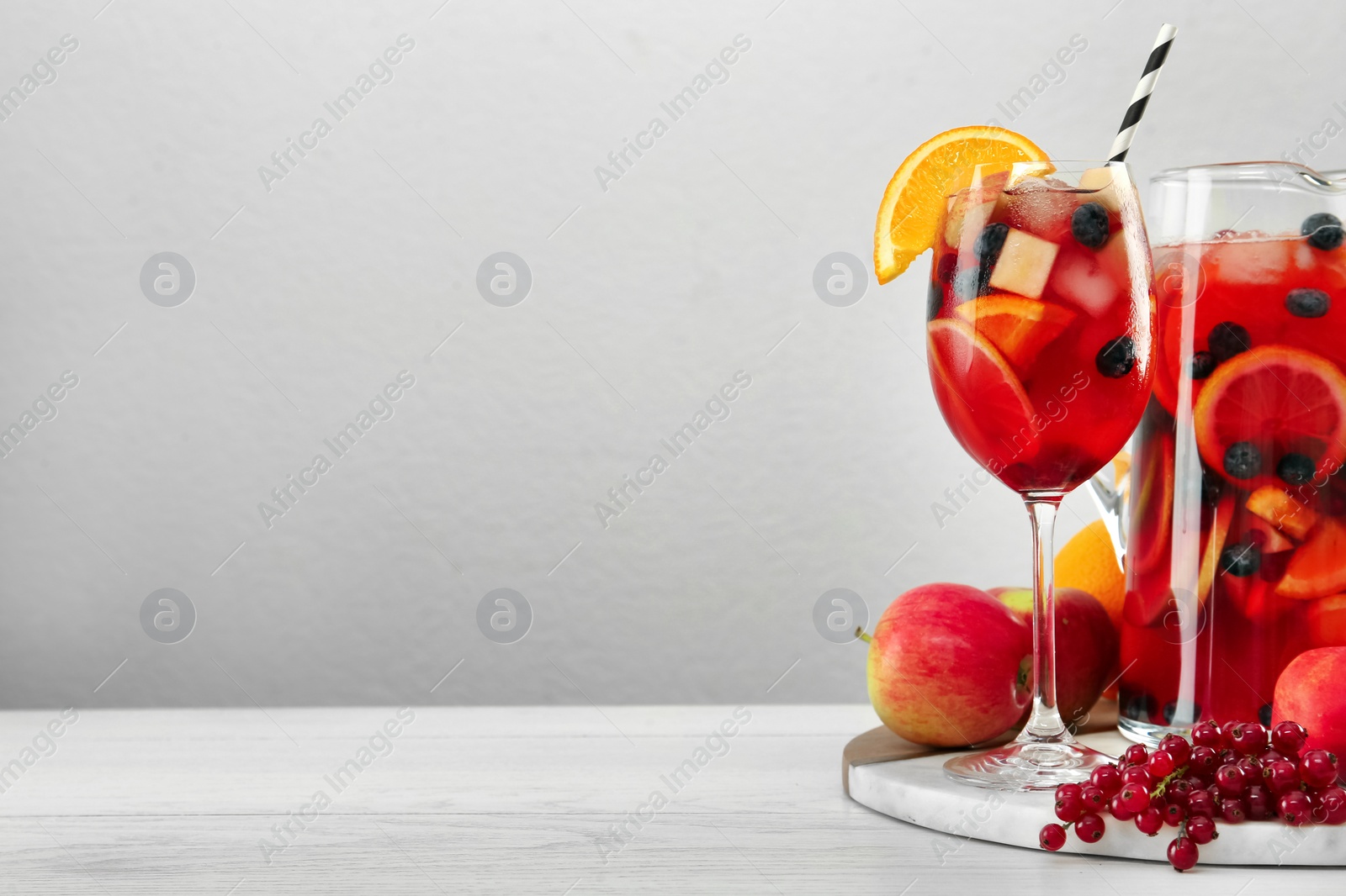 Photo of Glass and jug of Red Sangria on white wooden table against light grey background. Space for text