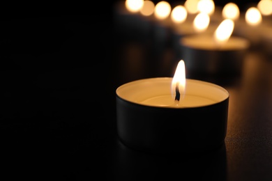 Photo of Burning candle on table in darkness, closeup with space for text. Funeral symbol