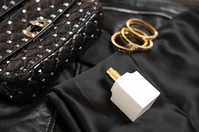 Leather bag, bottle of perfume and golden bracelets on black fabric, closeup