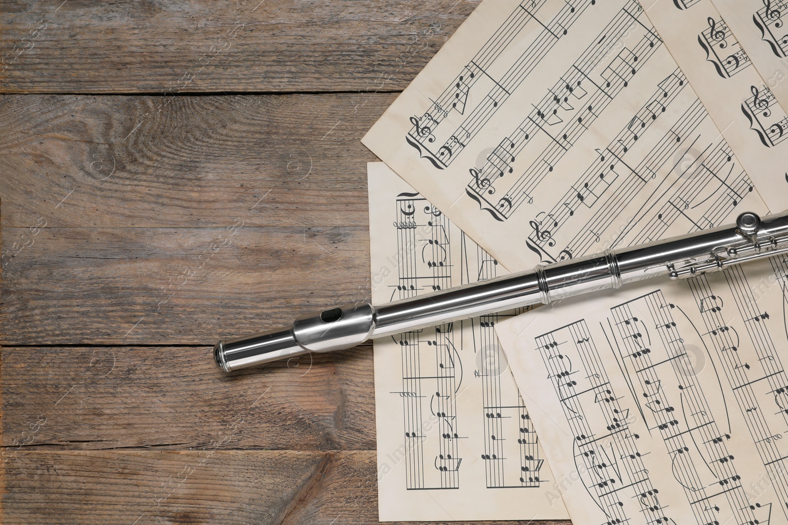 Photo of Sheets with musical notes and flute on wooden table, flat lay. Space for text