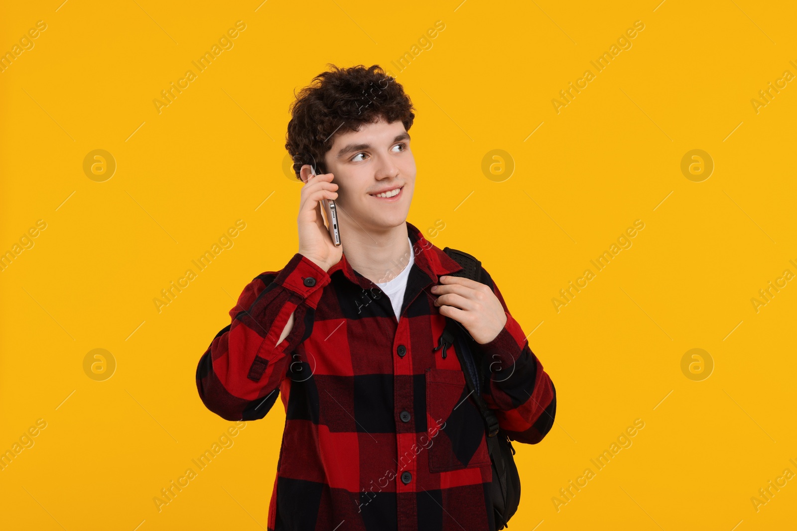 Photo of Portrait of student with backpack talking on smartphone against orange background