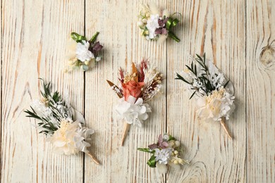 Photo of Stylish boutonnieres on light wooden table, flat lay