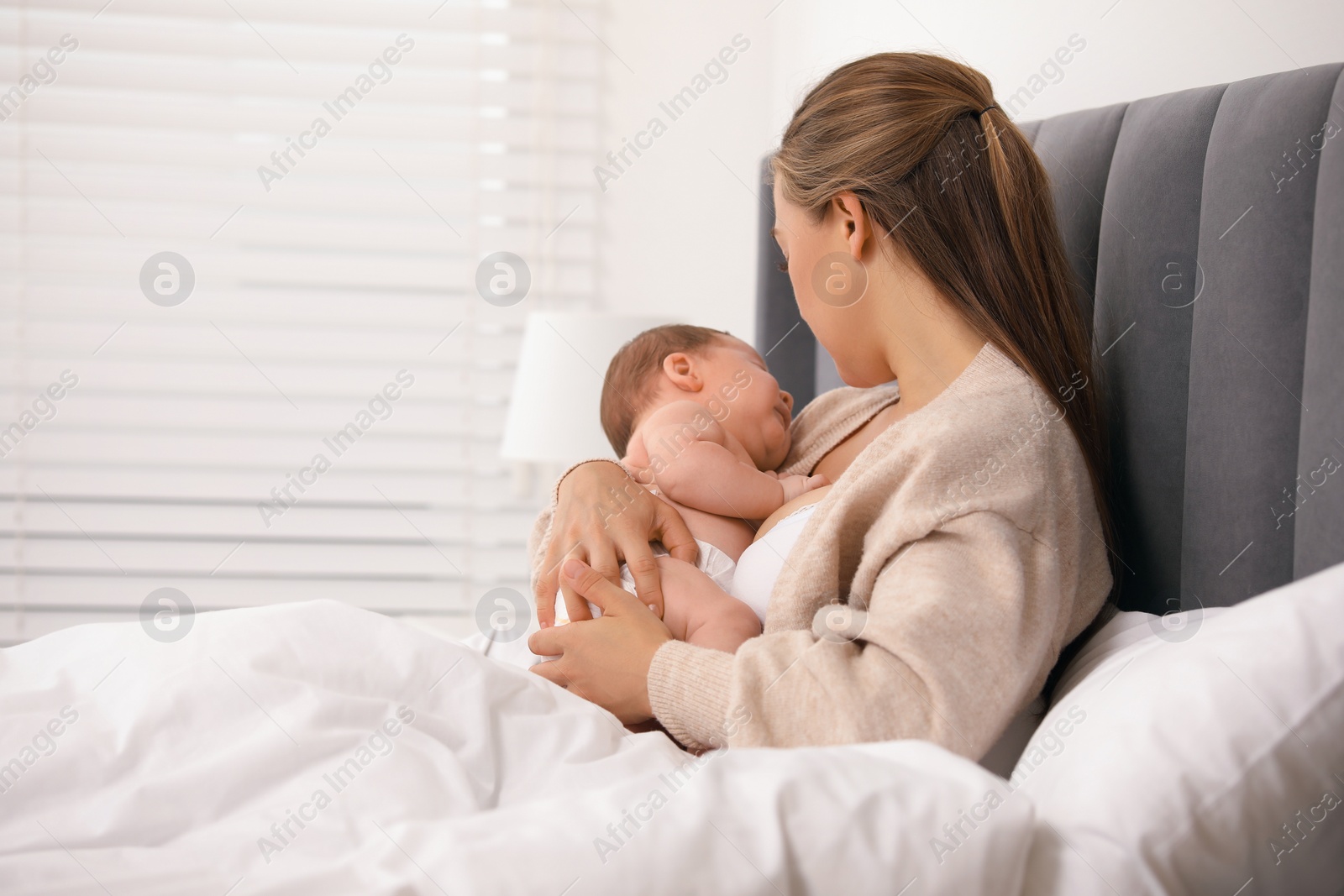 Photo of Mother holding her cute newborn baby in bed indoors, space for text