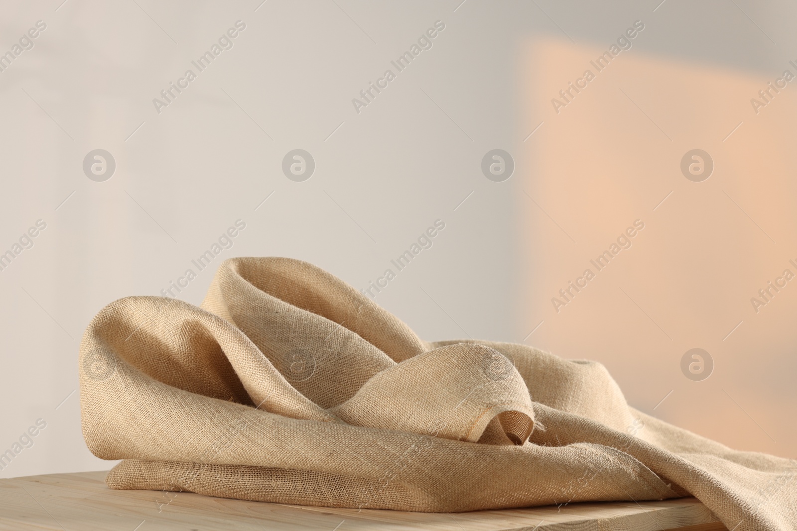 Photo of Natural burlap fabric on wooden table against light background. Space for text