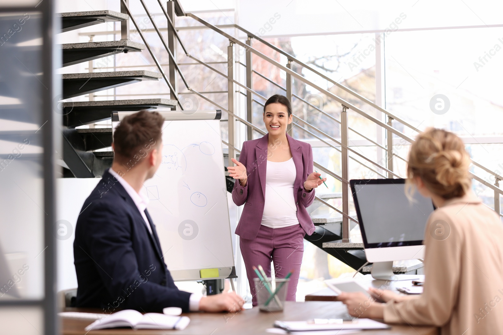 Photo of Young pregnant woman giving presentation to colleagues at workplace