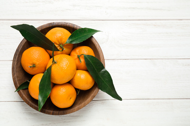 Fresh ripe tangerines with leaves and space for text on white wooden table, top view. Citrus fruit