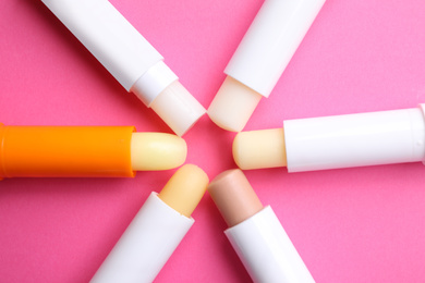 Photo of Hygienic lipsticks on pink background, flat lay