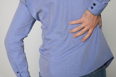 Man suffering from pain in back on light background, closeup. Arthritis symptoms