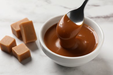 Taking yummy salted caramel with spoon from bowl on table, closeup