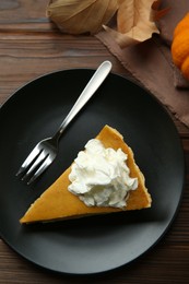 Piece of delicious pumpkin pie with whipped cream and fork on wooden table, top view