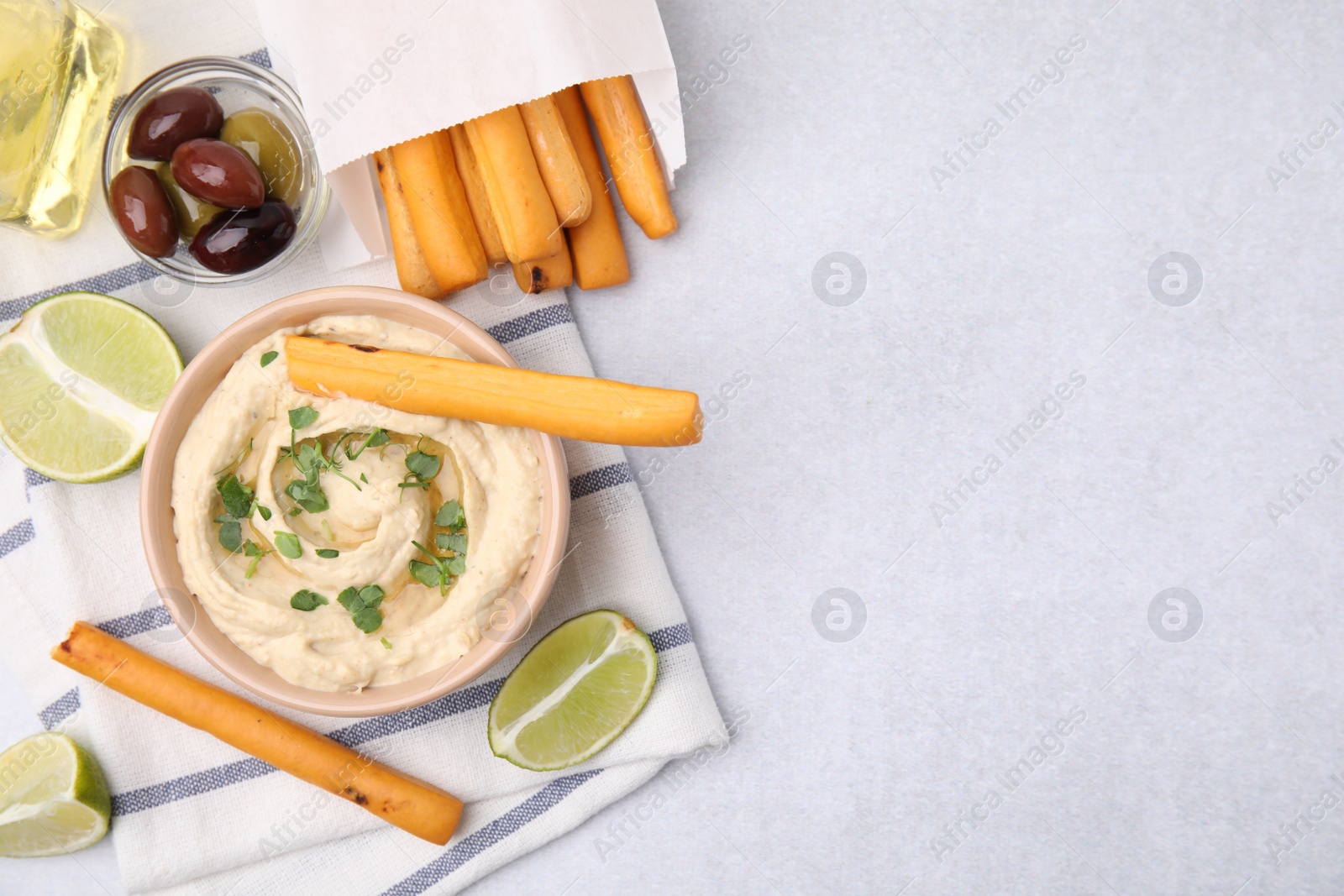 Photo of Delicious hummus with grissini sticks served on light grey table, flat lay. Space for text