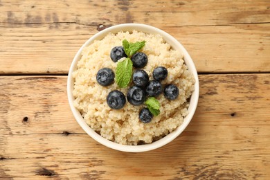 Photo of Tasty quinoa porridge with blueberries and mint in bowl on wooden table, top view