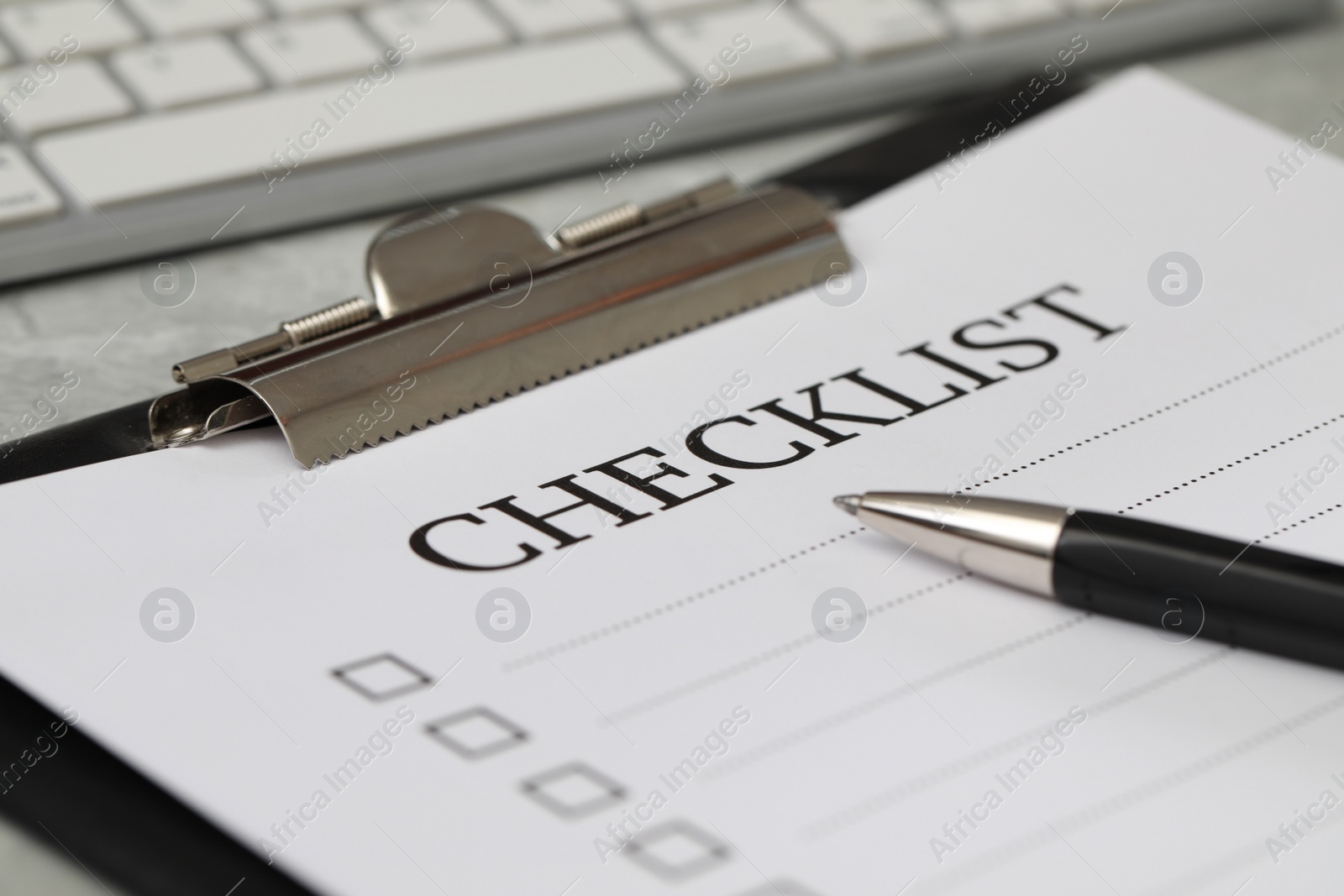 Photo of Clipboard with inscription Checklist and pen on grey table, closeup