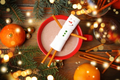 Flat lay composition with marshmallow snowman in cup of hot drink on wooden table. Bokeh effect 