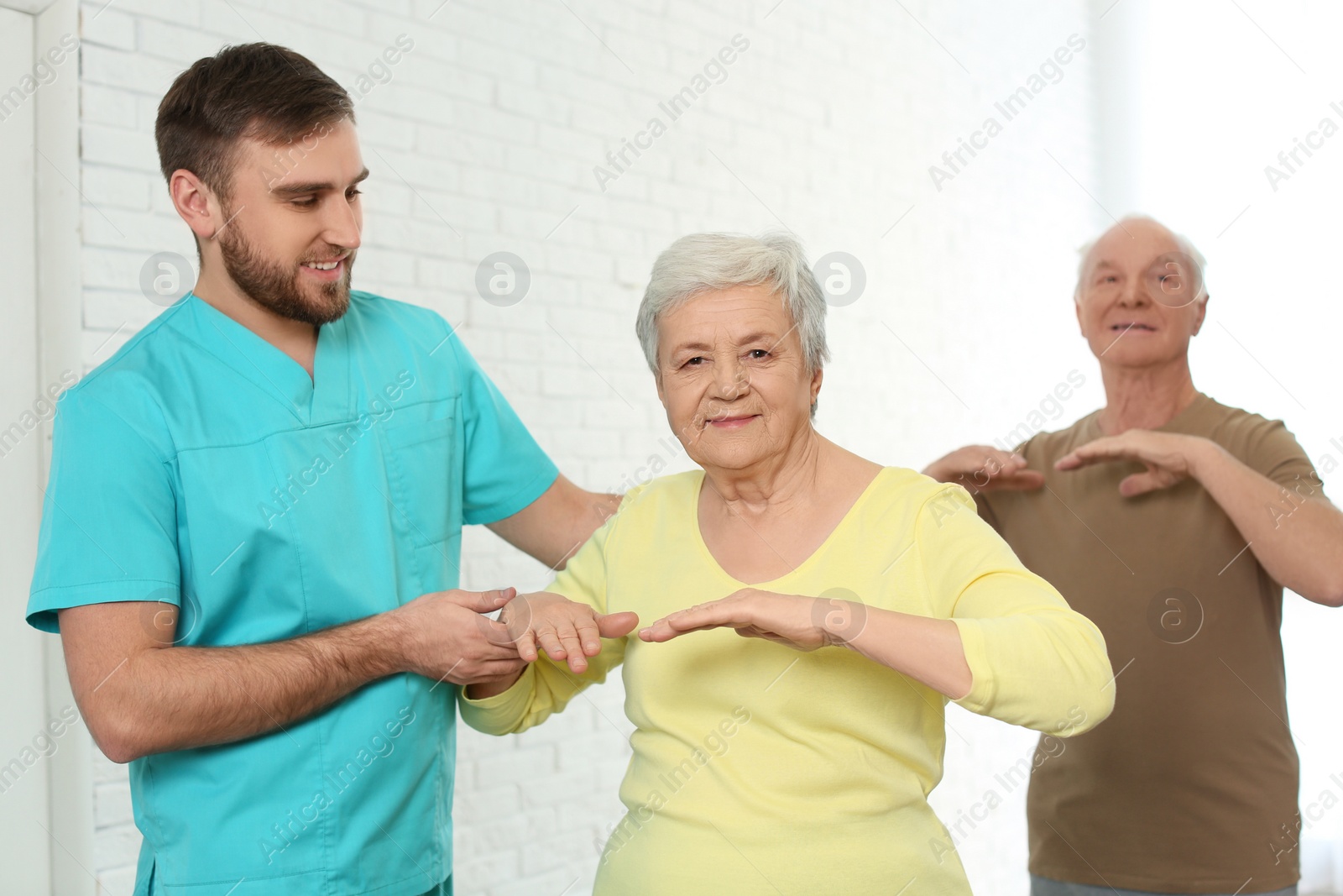 Photo of Care worker helping elderly woman to do sports exercise in hospital gym.