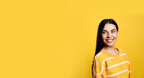 Photo of Portrait of happy young woman with beautiful black hair and charming smile on yellow background, space for text