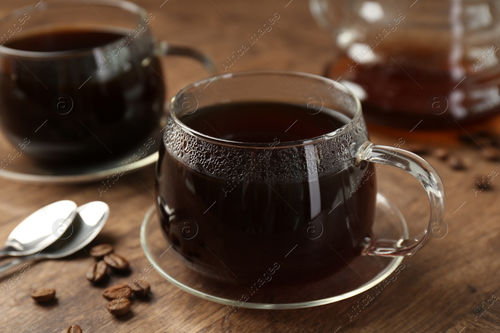 Photo of Hot coffee in glass cups, spoons and beans on wooden table, closeup