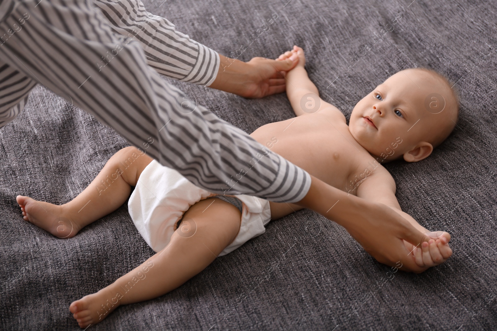 Photo of Young woman massaging cute little baby on blanket