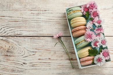 Photo of Delicious macarons and flowers on white wooden table, flat lay. Space for text