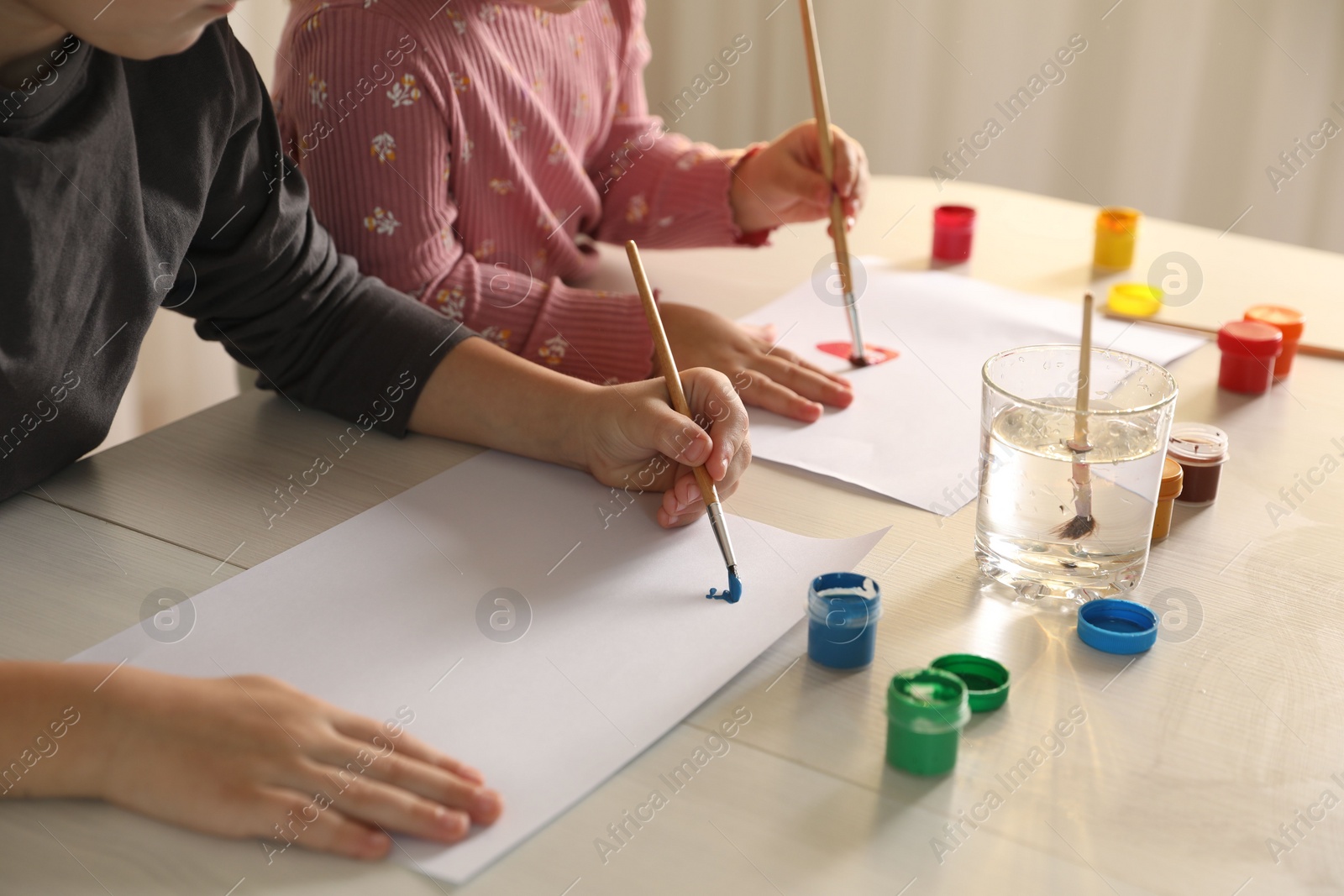 Photo of Little children drawing with brushes at wooden table indoors, closeup