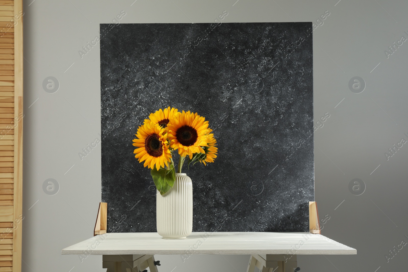 Photo of Vase with beautiful sunflowers and double-sided backdrop on table in photo studio