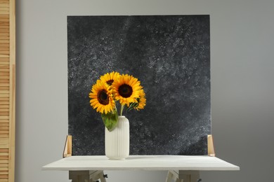 Photo of Vase with beautiful sunflowers and double-sided backdrop on table in photo studio