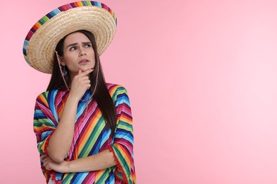 Photo of Thoughtful woman in Mexican sombrero hat and poncho on pink background. Space for text