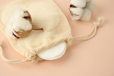 Photo of Bag with cotton pads and flowers on beige background, closeup