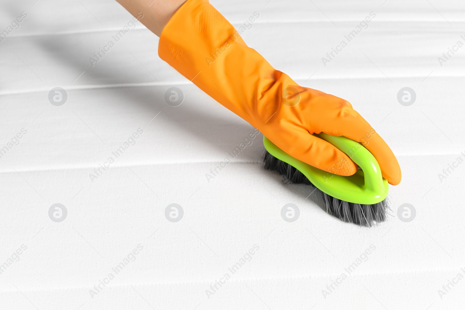 Photo of Woman in orange gloves cleaning white mattress with brush, closeup. Space for text