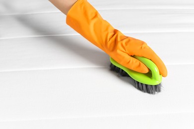 Woman in orange gloves cleaning white mattress with brush, closeup. Space for text