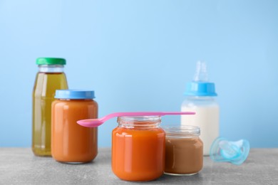 Jars with healthy baby food, milk, juice and pacifier on light grey table