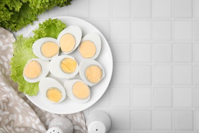 Photo of Fresh hard boiled eggs and lettuce on white tiled table, top view. Space for text