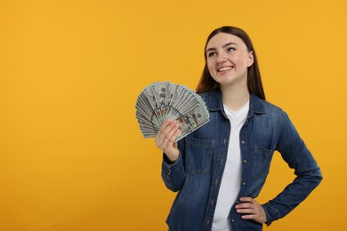 Happy woman with dollar banknotes on orange background, space for text