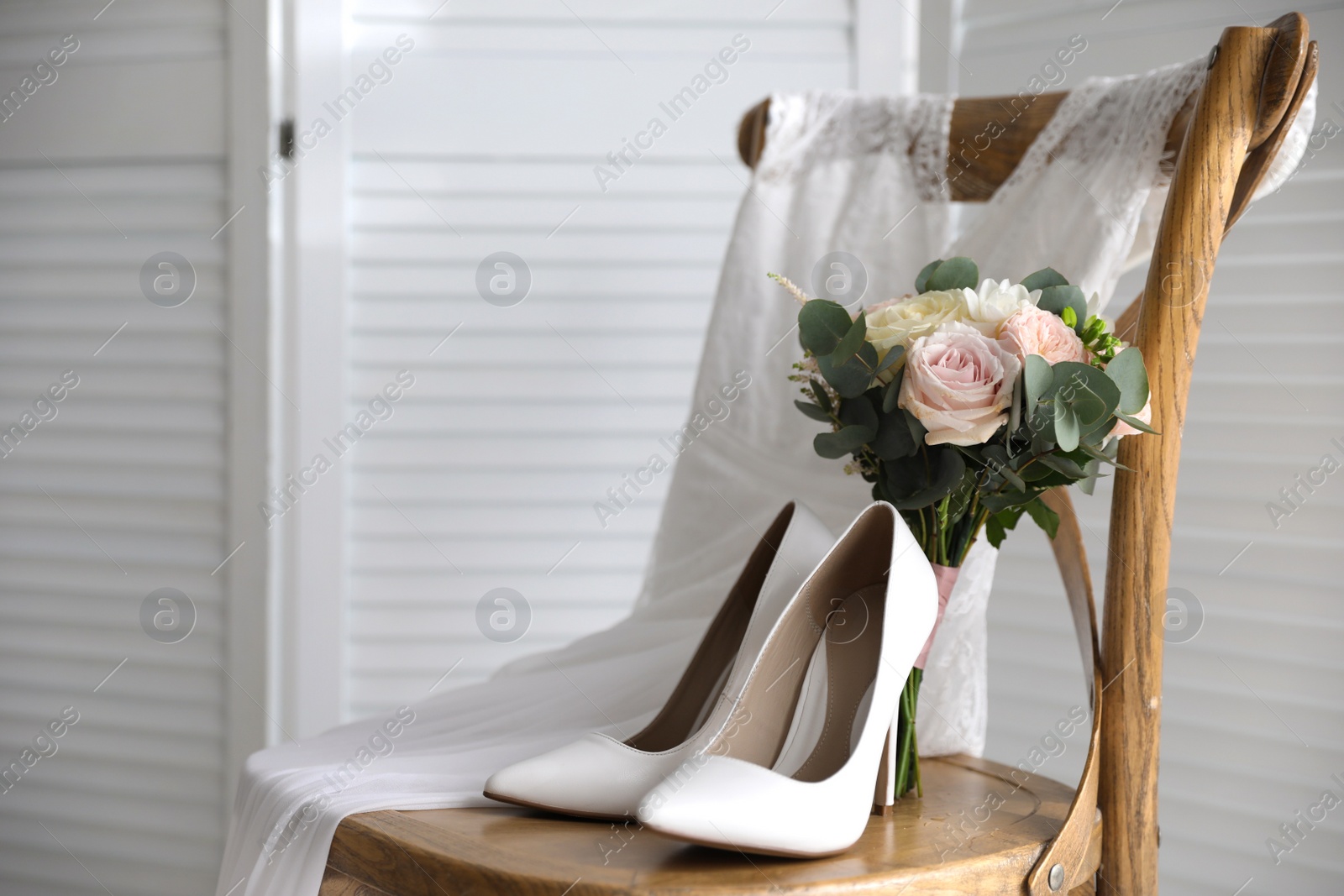 Photo of White high heel shoes, flowers and wedding dress on wooden chair indoors. Space for text