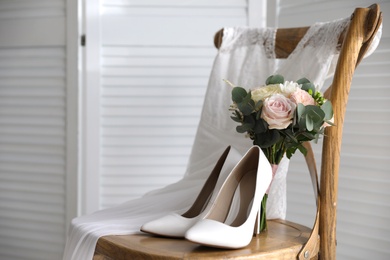 Photo of White high heel shoes, flowers and wedding dress on wooden chair indoors. Space for text