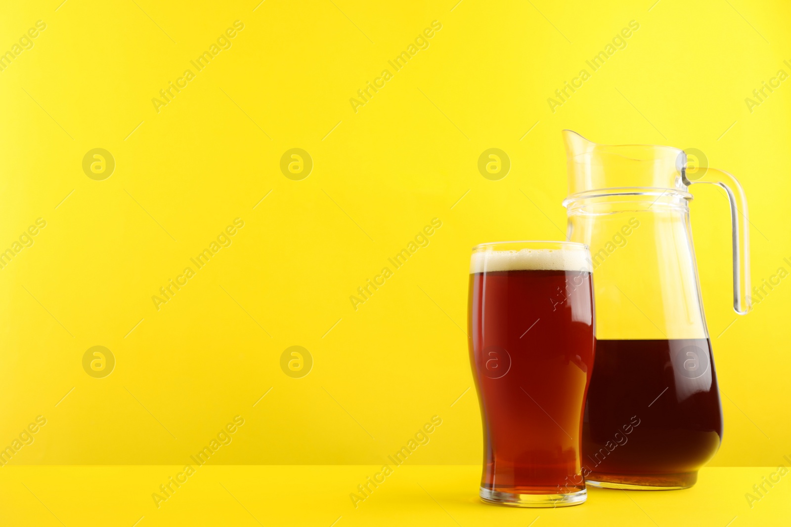 Photo of Delicious homemade kvass in glass and jug on yellow background. Space for text