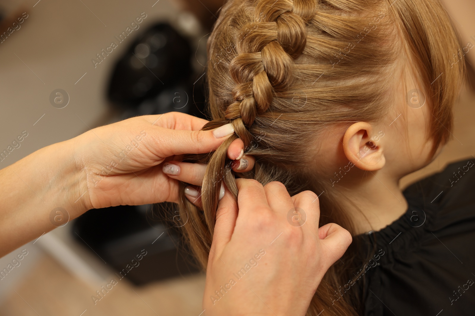 Photo of Professional hairdresser braiding girl's hair in beauty salon, closeup