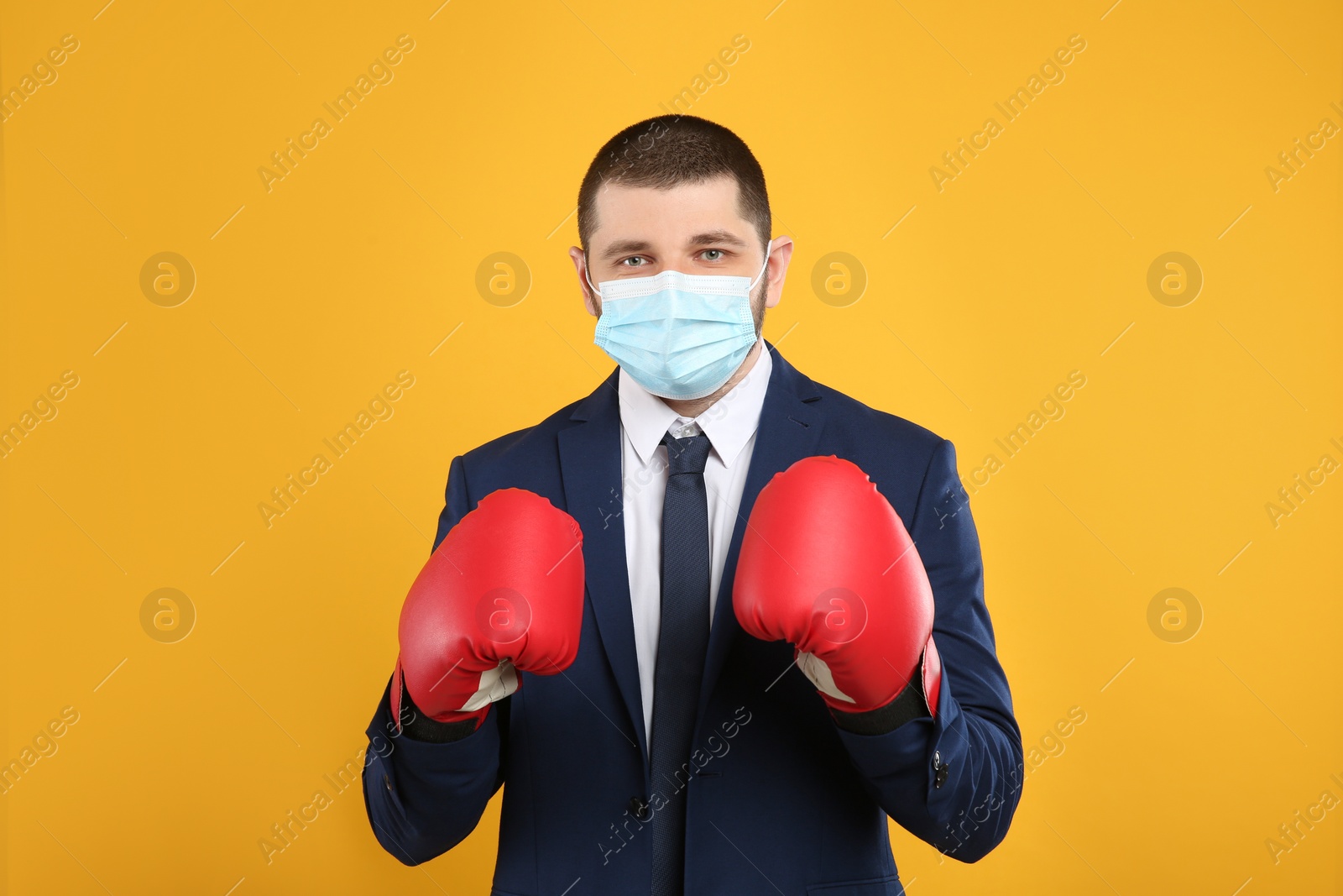 Photo of Businessman with protective mask and boxing gloves on yellow background. Strong immunity concept