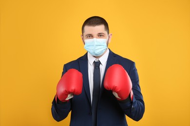 Businessman with protective mask and boxing gloves on yellow background. Strong immunity concept