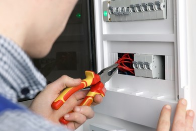 Photo of Professional repairman fixing electric panel with pliers indoors, closeup