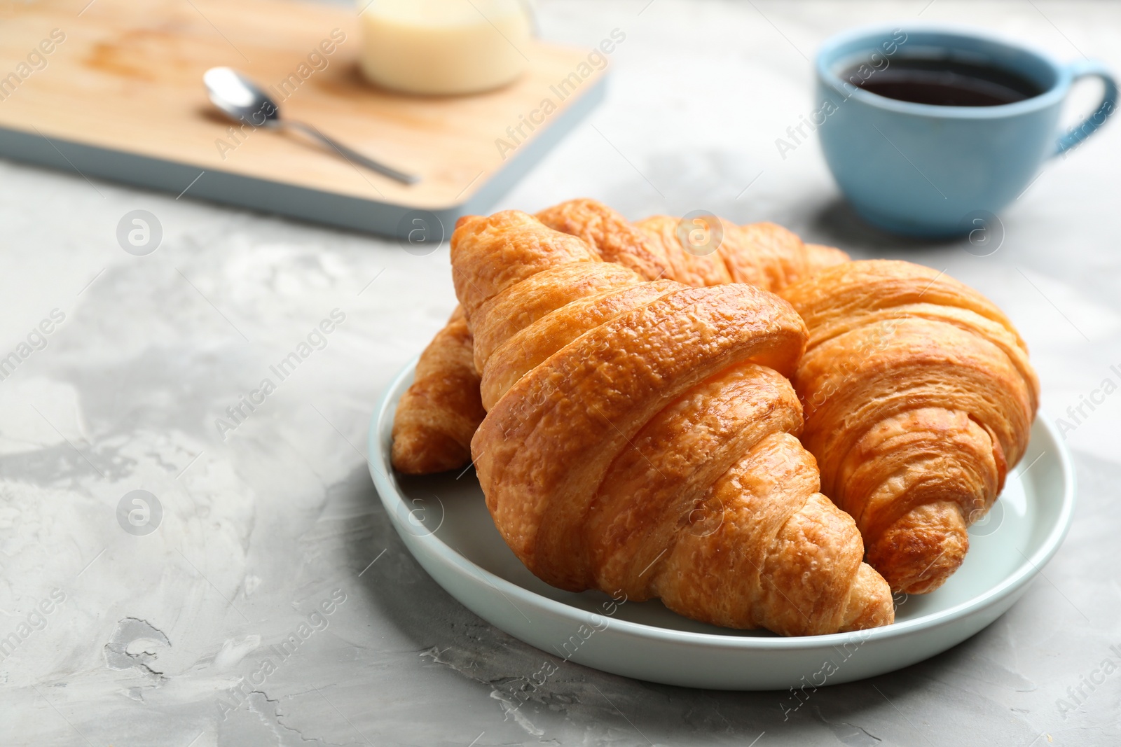 Photo of Plate of fresh croissants on grey table, space for text. French pastry