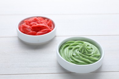 Photo of Bowls with swirl of wasabi paste and pickled ginger on white wooden table, closeup