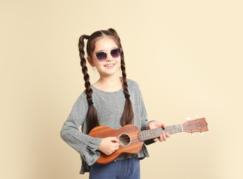 Portrait of little cheerful girl playing guitar on color background
