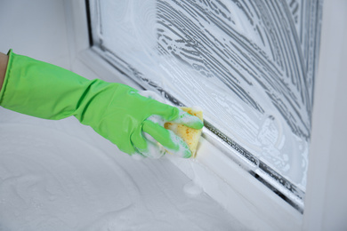 Woman cleaning window with sponge indoors, closeup