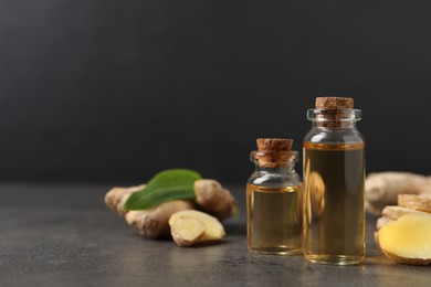 Photo of Glass bottles of essential oil and ginger root on grey table, space for text