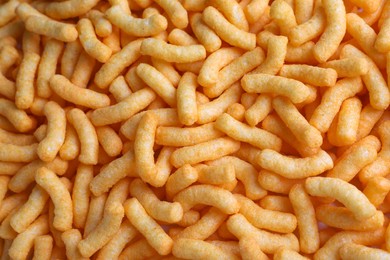 Photo of Many crunchy cheesy corn puffs as background, top view