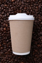 Photo of Coffee to go. Paper cup on roasted beans, top view