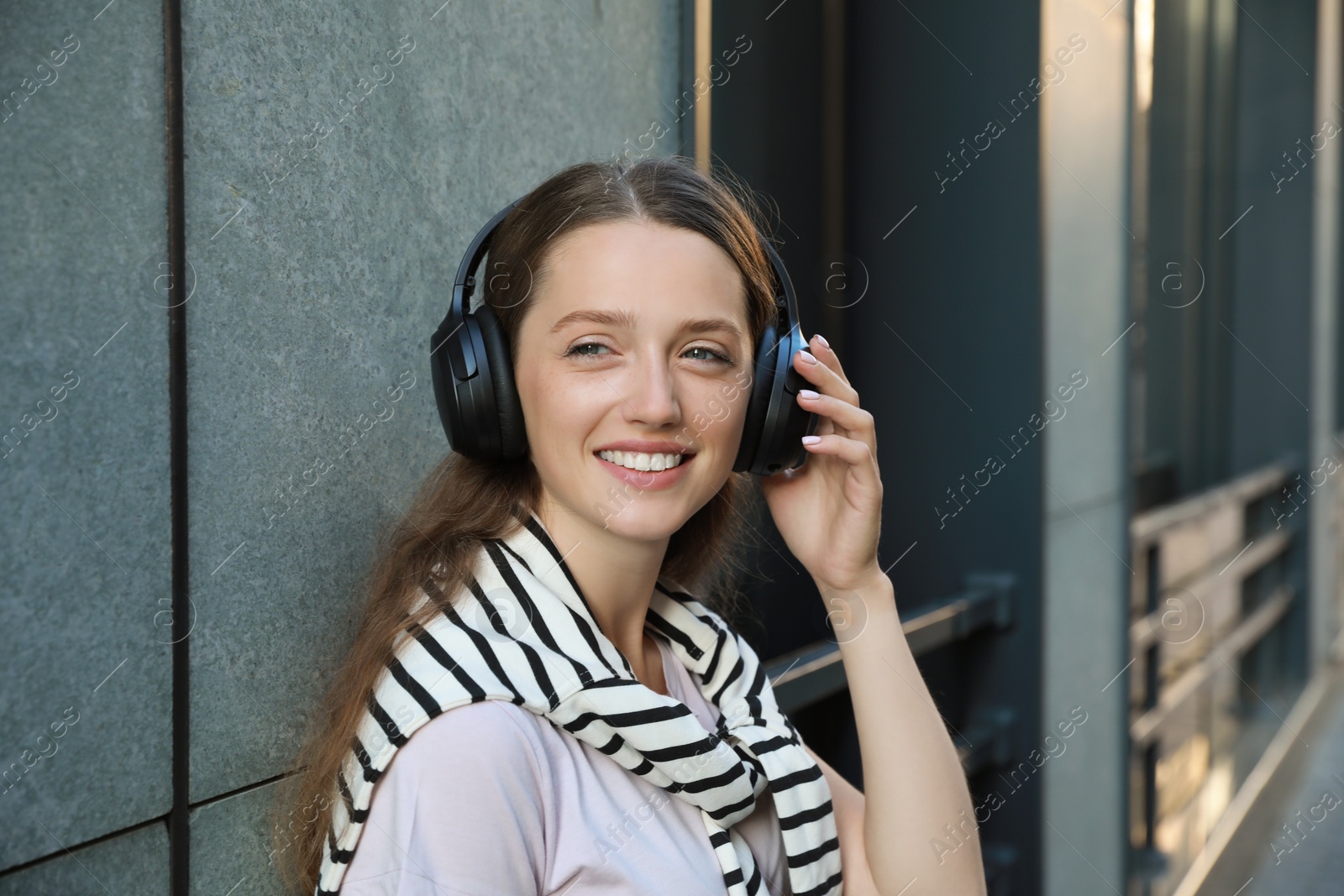 Photo of Smiling woman in headphones listening to music near building outdoors