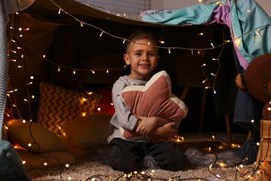 Photo of Happy boy with star shaped pillow in decorated play tent at home