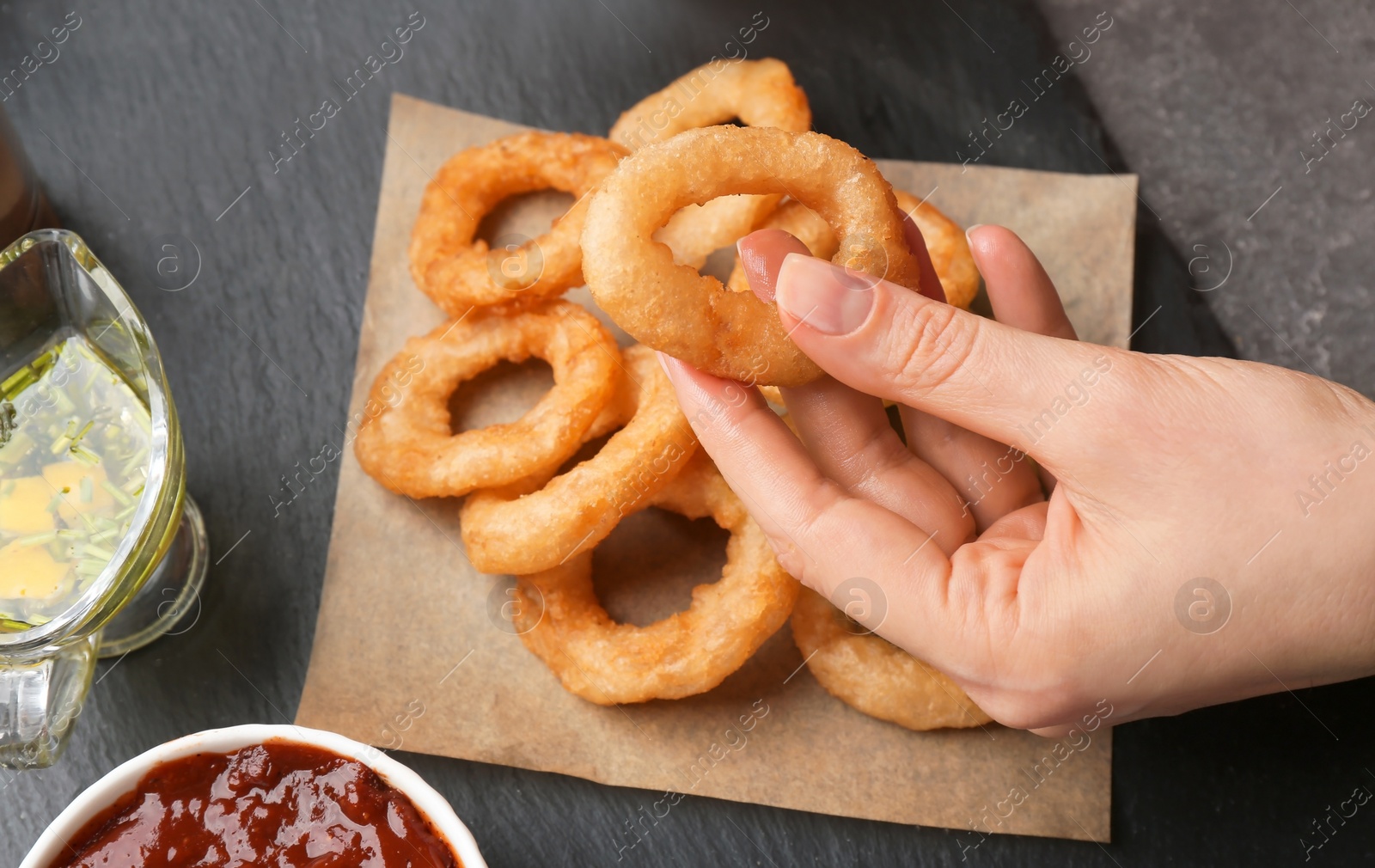 Photo of Woman eating fried onion rings with sauce at table